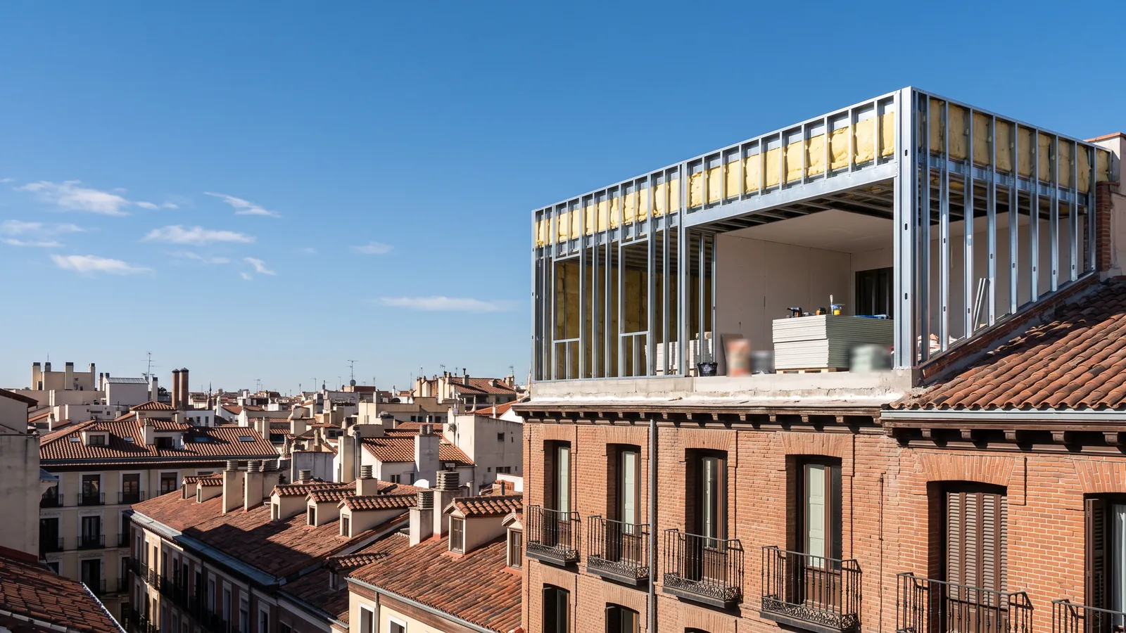 Remonta en construcción en seco sobre un edificio de ladrillo de Madrid: estructura de acero galvanizado con aislamiento y placas de yeso laminado, y los tejados de la ciudad al fondo
