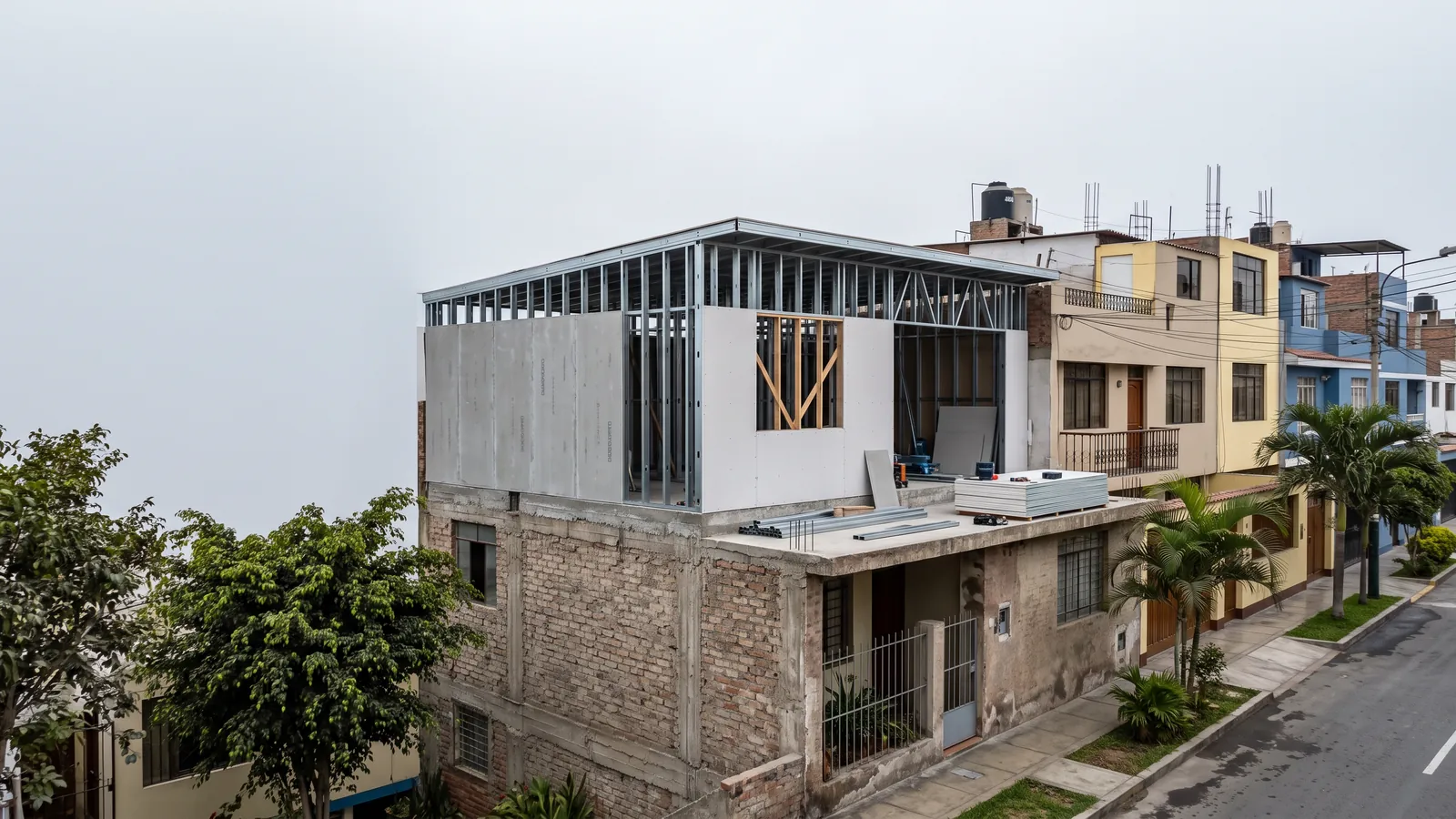Segundo piso en construcción con perfiles de acero galvanizado y placas sobre el techo de una casa de ladrillo, en una calle de Miraflores (Lima) bajo el cielo gris de la garúa